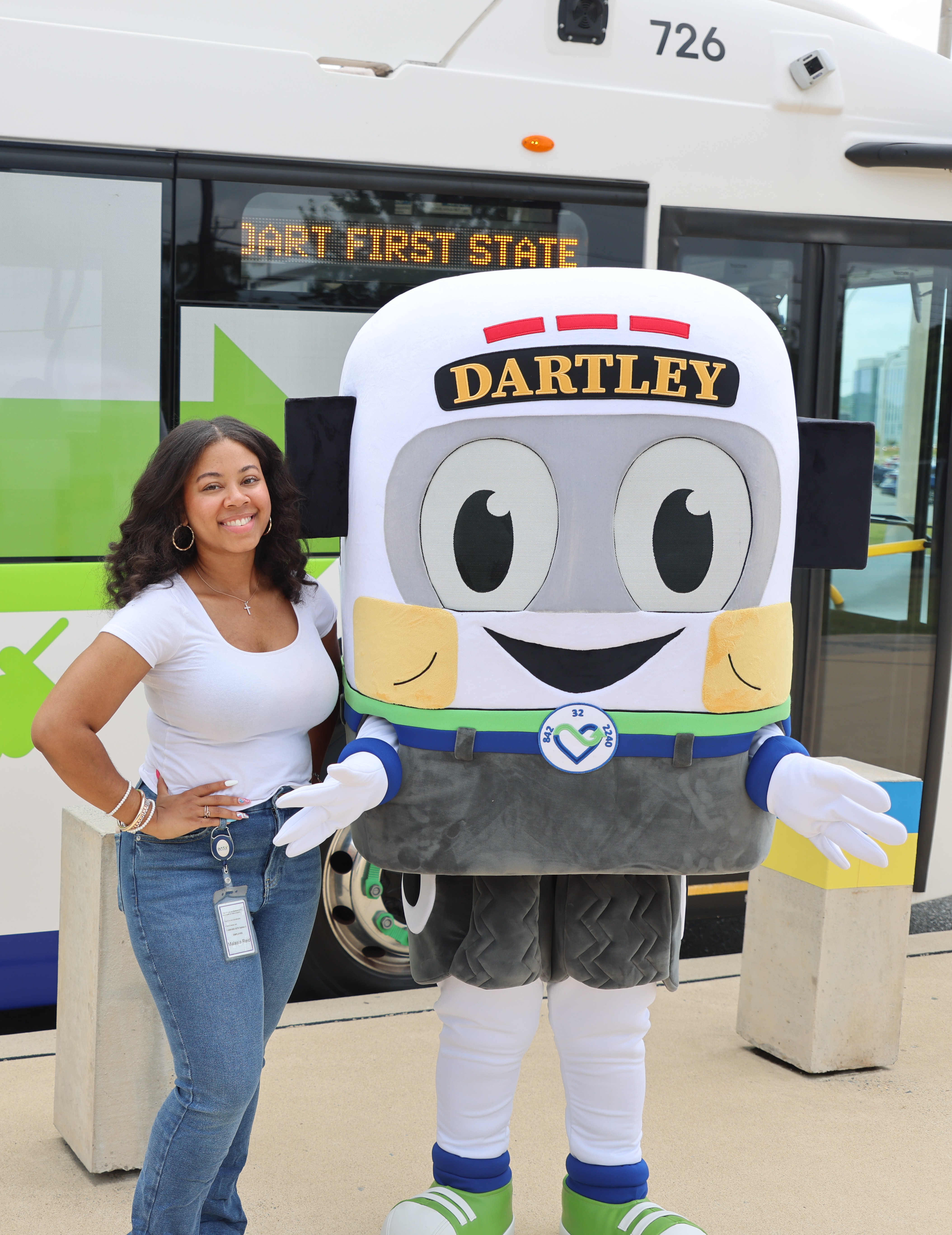 Malasia Reid standing beside the DARTLEY mascot costume in 
                front of a DART bus.